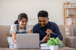 © wichayada - Happy couple using credit card to make online purchases on laptop in living room.