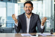 © Liubomir - Webcam view video call, young arab man inside office talking with colleagues remotely, man looking at camera smiling at workplace inside office.