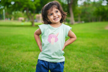 Happy cute little indian girl child standing having fun at summer park or garden.