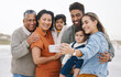 © Wesley/peopleimages.com - Family, grandparents and children in selfie on beach for holiday, vacation and outdoor on social media. Happy mother, father and senior people with interracial kids in profile picture or photography