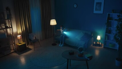 Wall Mural - Video of a young woman sitting on a couch in a dark room looking around for burglars, intruders, thieves. She holds a baseball bat and a flashlight and calls emergency hotline.