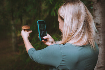 The person takes mobile photo of mushroom in her hand during mushrooming in the forest