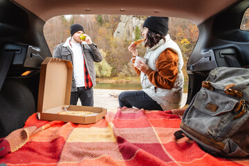 Poster - couple sitting in car trunk having picnic resting at nature