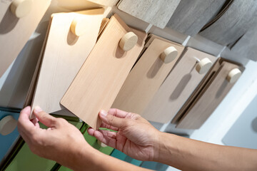Wall Mural - Designer hand picking wood samples board from material swatch wall display in material library. Choosing wooden laminate texture in beige tone collection for interior architecture or furniture design