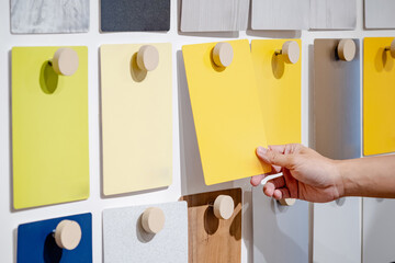Wall Mural - Designer hand picking yellow laminate sheet on material swatch wall display in material library. Choosing color board from collection for interior architecture and furniture finishing design