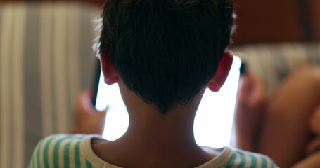 Back of child head staring at screen device at night