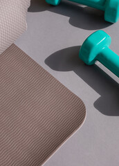 Sport or workout concept flat lay with blue dumbbells, yoga mat on the grey background. Copy space