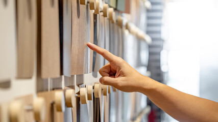 Wall Mural - Designer hand pointing wood samples board on material swatch wall display in library. Choosing wooden laminate texture in brown and beige tone collection for interior architecture or furniture design