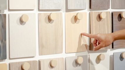 Wall Mural - Designer hand pointing wood samples board on material swatch wall display in library. Choosing wooden laminate texture in brown and beige tone collection for interior architecture or furniture design