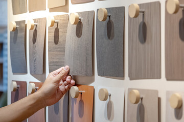 Wall Mural - Designer hand picking wood samples board from material swatch wall display in material library. Choosing wooden laminate texture in brown tone collection for interior architecture or furniture design