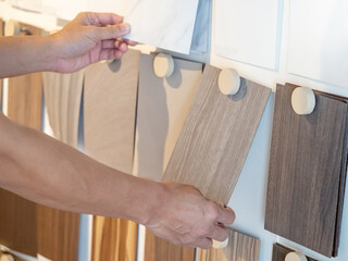 Wall Mural - Designer hand picking wood samples board from material swatch wall display in material library. Choosing wooden laminate texture in beige tone collection for interior architecture or furniture design