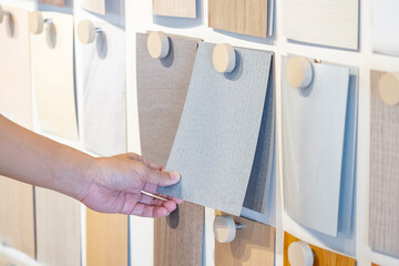 Wall Mural - Designer hand picking wood samples board from material swatch wall display in material library. Choosing wooden laminate texture in gray tone collection for interior architecture or furniture design