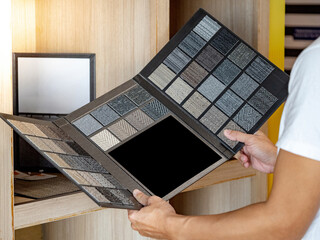 Wall Mural - designer hand holding fabric tile carpet samples catalog in material library. choosing rug flooring 