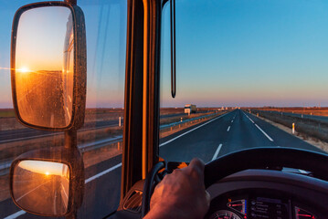 Poster - View from the driver's seat of a truck, with a straight road ahead and the sun rising in the rearview mirror.