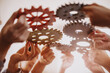 People's hands joining different metall cog wheel together.