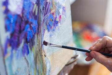 Senior woman's hands using a brush painting an oil painting with out of focus background