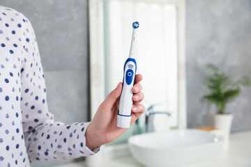 Wall Mural - Woman holding electric toothbrush in bathroom at home, closeup