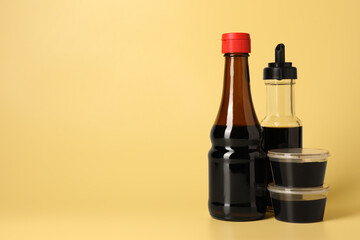 Wall Mural - Bottles and bowls with soy sauce on yellow background, space for text