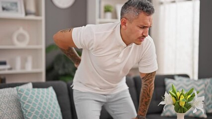 Sticker - Young hispanic man suffering for backache sitting on sofa at home