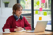 © PHAISITSAWAN - Beautiful Asian businesswoman sitting at a table with computer wearing headphones with microphone Looking at the laptop camera Happy businesswoman educating customers online.