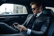© AspctStyle - Handsome businessman sitting in luxury car and texting with client on phone, Young attractive businessman in formal using smartphone while sitting on back seat of business car