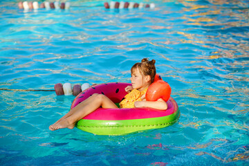 Happy little girl with inflatable toy ring float in swimming pool. Little preschool child learning to swim and dive in outdoor pool of hotel resort. Healthy sport activity and fun for children.