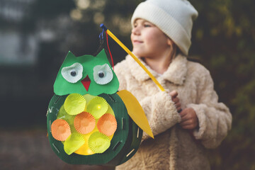 Little preschool kid girl holding selfmade traditional owl lanterns with candle for St. Martin procession. child happy about children and family parade in kindergarten. German tradition Martinsumzug