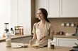 © fizkes - Happy dreamy pretty young woman cooking homemade breakfast in kitchen, beating fresh milk and eggs for omelet in bowl, looking away, smiling, laughing, enjoying culinary activities