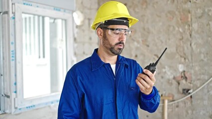 Wall Mural - Young hispanic man worker talking on walkie-talkie at construction site