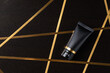 Black cosmetic squeeze tube on black table decorated with golden stripe line.