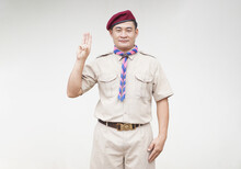 Handsome Asian Man Wear Boy Scout Uniform, Red Cap, Blue And Pink Striped Scarf, Make Hand Sign Symbol Of Scout. Concept, Educational Career With Uniform In School, Thailand.  