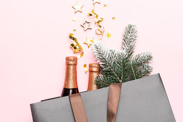 Wall Mural - Festive New Year and Christmas composition with champagne bottles and fir tree branches in a paper bag on light pink background top view. Christmas sale and promo banner.