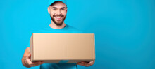 Young Courier, The Delivery Man, Holds An Empty Cardboard Box Isolated On Blue Background