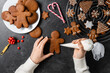 © Syda Productions - baking, cooking, christmas and food concept - close up of hands with pastry bag decorating gingerbread cookies with white icing on black table top