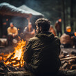Man from behind sitting at the campfire with a few people around in motion blur