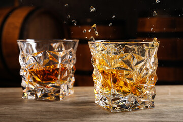 Poster - Glasses with whiskey on table against wooden barrels, closeup