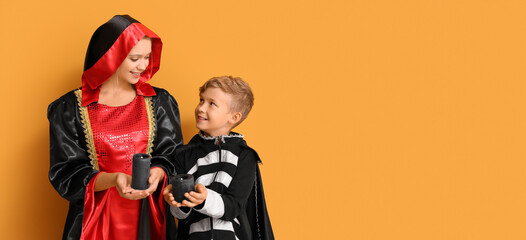 Sticker - Mother and little son in Halloween costumes and with candles on orange background with space for text