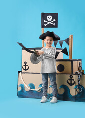 Poster - Cute little pirate with sword and cardboard ship on blue background