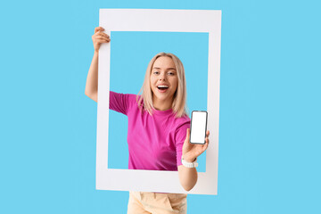 Poster - Young beautiful happy woman with frame and mobile phone on blue background