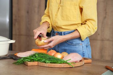 Young woman peeling potato for chicken soup in kitchen, closeup