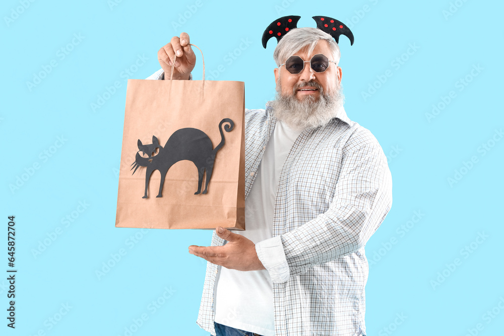 Mature man dressed for Halloween with gift bag on blue background