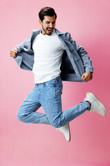 Poster - Man with beard jumping on pink background in white T-shirt and jeans, smile and joyful emotion on his face, full-length, copy space