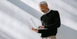 © gstockstudio - Confident mature man in smart casual wear using laptop while standing against a wall