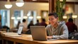 © Karolis - Focused student studying at a wooden table in a cozy library. Smiling, determined, with warm lighting and a laptop. Books, laptop, and a peaceful atmosphere.