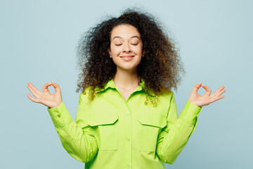 Canvas Print - Young spiritual tranquil latin woman wear green shirt casual clothes hold spreading hands in yoga om aum gesture relax meditate try to calm down isolated on plain pastel light blue cyan background.