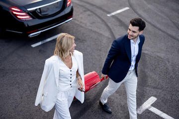 Business couple walking with a suitcase on parking lot, arrived by luxury taxi, view from above. Concept of transportation and business trips