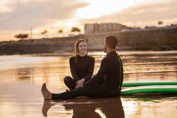 Wall Mural - Happy Young Couple Relaxing On The Beach After Surfing Together