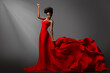 Beautiful Woman dancing in Red waving Dress on Stage. Fashion Dark Skin Model in long Gown Side View. Stylish Girl with Afro hair Style over Gray Background