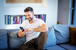 © sepy - Confident man relaxing at home and using smartphone