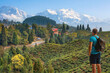 Male tourist looks on at the scenic Himalayan landscape with view of tea plantations and the Kanchenjunga Himalaya mountain range in the background at Tinchuley, Darjeeling India